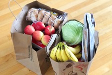 two paper bags of food, including apples, bananas, bagels, cabbage and bread