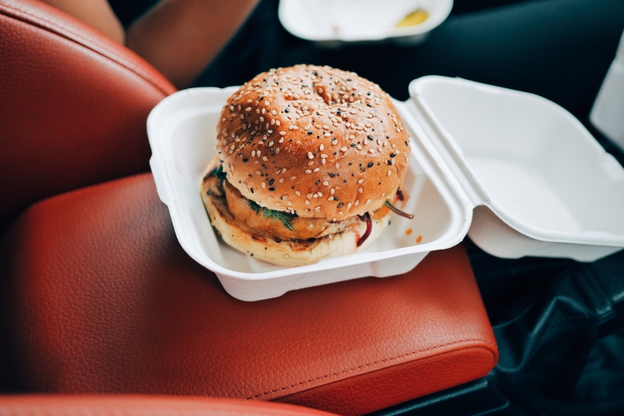 Burger in a white takeaway box on a red leather seat